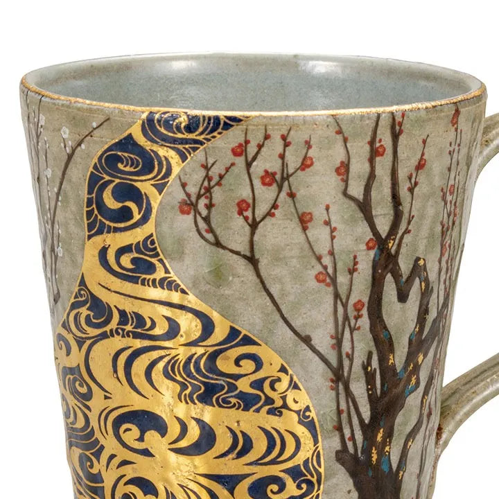 Ceramic mug with gold and blue decorative elements and a tree design.