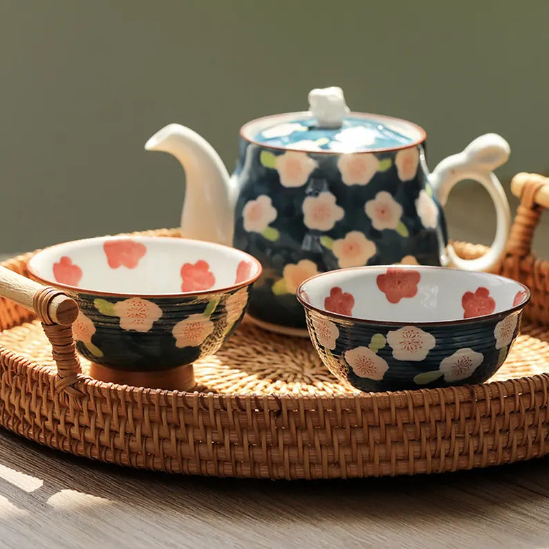 Ceramic teapot and bowls with floral design on a woven tray