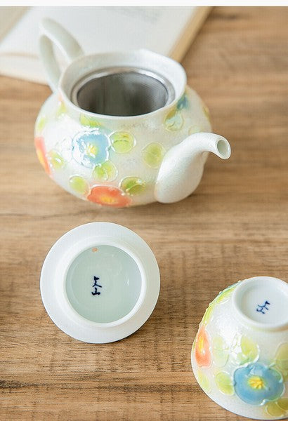 Ceramic teapot and cups with floral designs on a wooden surface