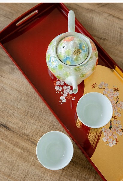 Tea set with a decorative teapot and cups on a wooden tray.