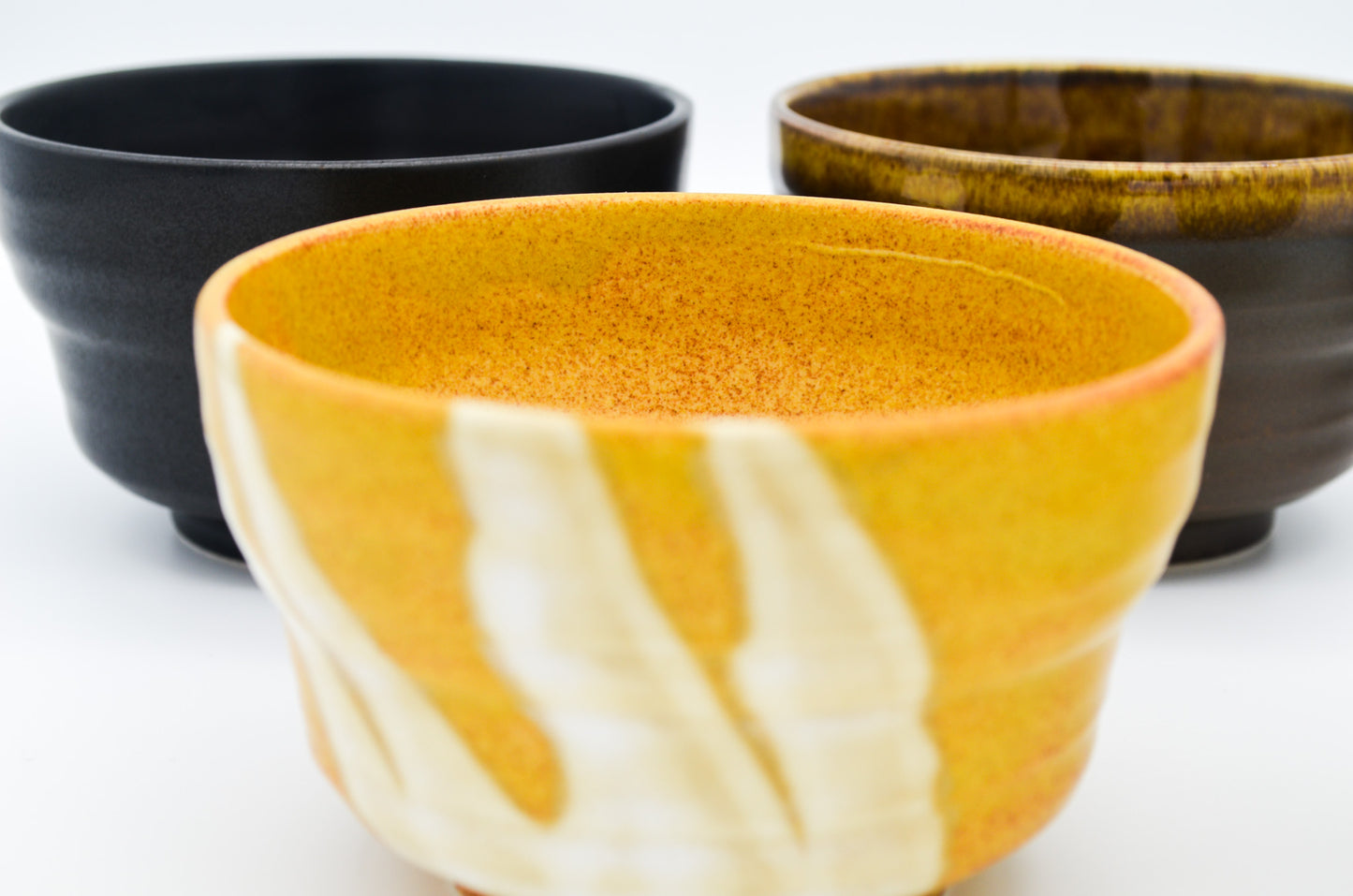Three ceramic bowls in black, orange, and brown on a white background