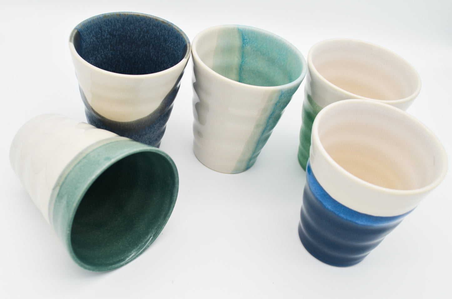 Set of five ceramic cups with blue and green glaze on a white background