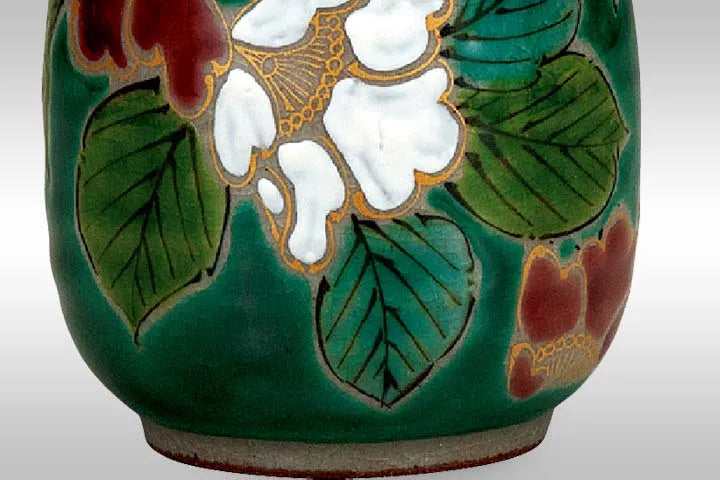 Ceramic teacup with green camellia floral design on a green background