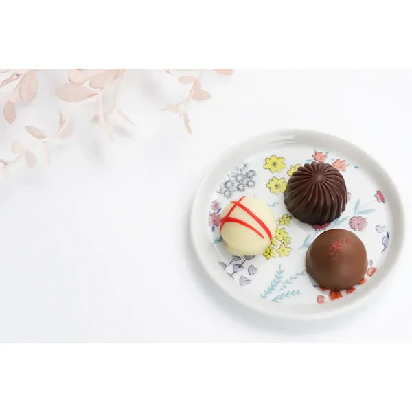 Three chocolate truffles on a decorative plate with floral patterns.