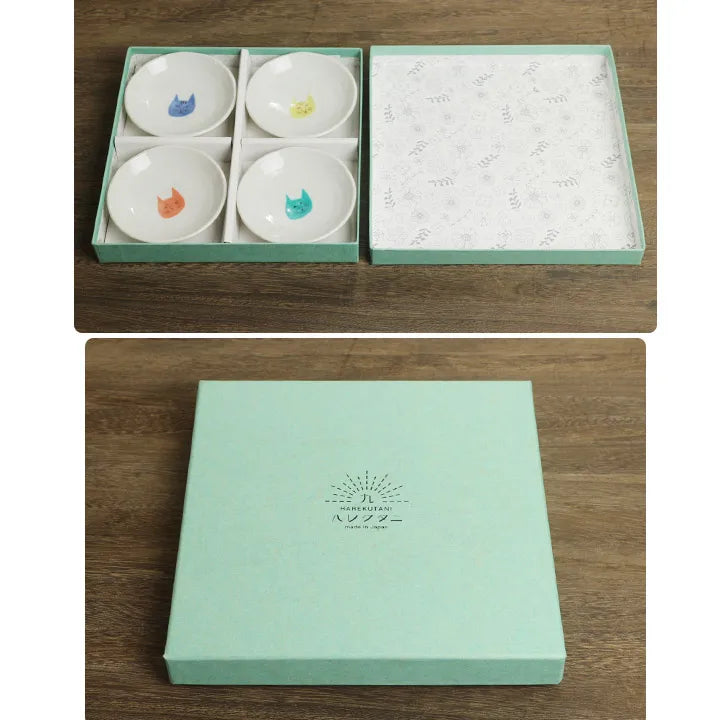 Set of four small ceramic bowls with colorful designs in a green box on a wooden surface.