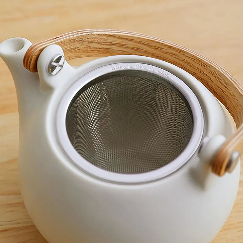 White teapot with wooden handle and lid on a wooden surface