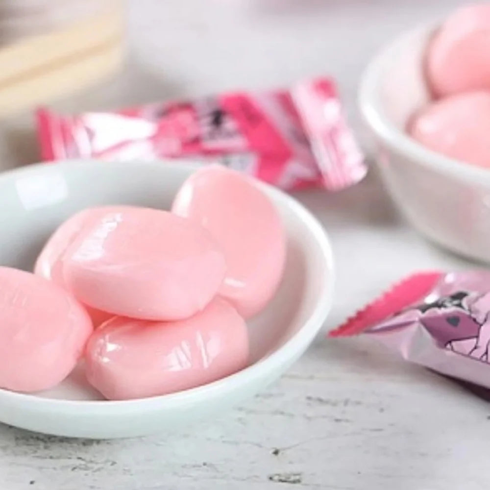 Pink gummy candies in a white bowl with a pink packaging in the background.