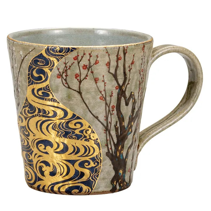 Ceramic mug with artistic design featuring gold patterns and a tree branch with plum blossoms on a greyish green background.