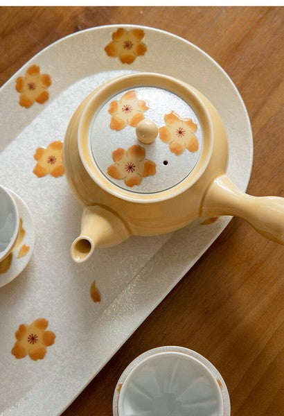 Ceramic teapot with floral design on a matching tray on a wooden surface