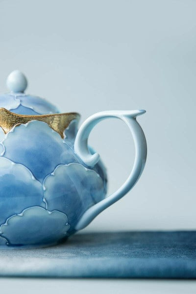 Blue ceramic teapot with gold accents on a light blue background