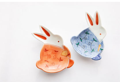 Two ceramic rabbit-shaped bowls, one orange and one blue, on a white background.