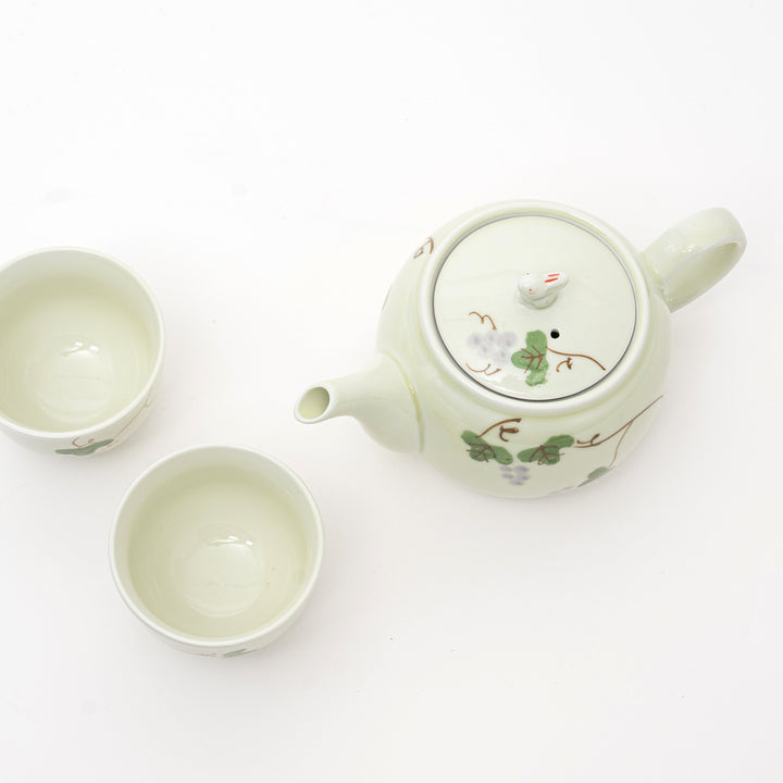 Ceramic teapot and two cups with floral designs on a white background