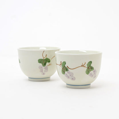 Two white ceramic cups with grapevine designs on a white background