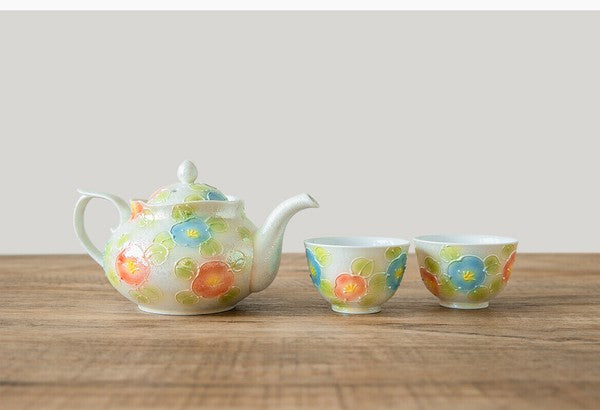 Teapot and two cups with floral design on a wooden surface