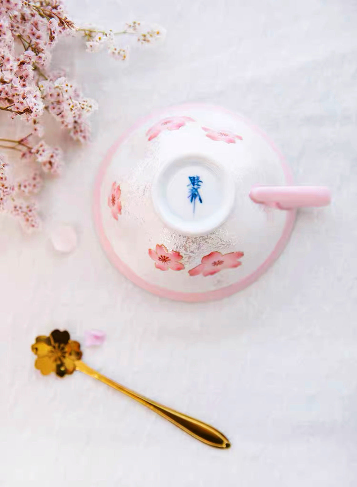 Ceramic bowl with floral design on a white surface with cherry blossoms and a spoon.