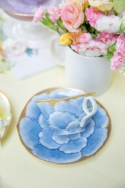 Ceramic teacup with floral design on a saucer, placed on a light surface with flowers in the background.
