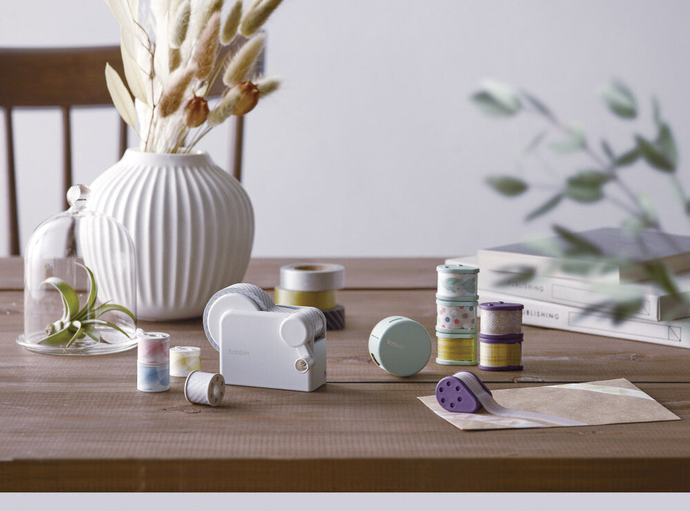 Spools of thread and sewing accessories on a wooden table with a vase and books in the background.