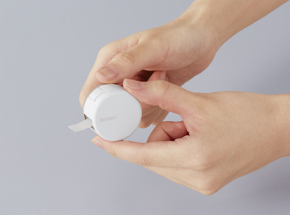 Hand holding a small white device with a brand name on a gray background