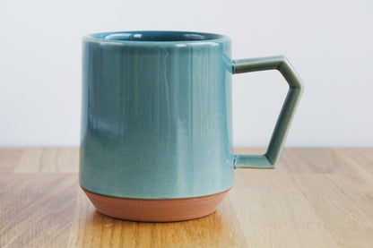 Teal ceramic mug on a wooden surface with a white background. Japanese Ceramic. Made in Japan