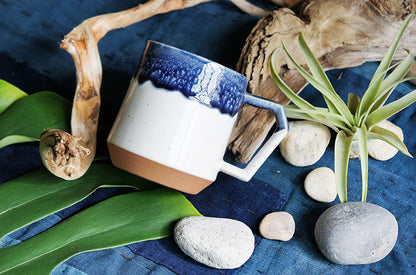 Ceramic mug with blue and white design on a blue surface with stones and plants. Japanese Ceramic. Made in Japan