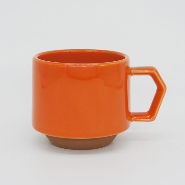 Orange ceramic mug with a brown base on a light gray background