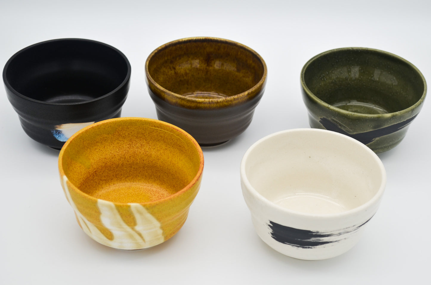 Five ceramic bowls of different colors and designs on a white background