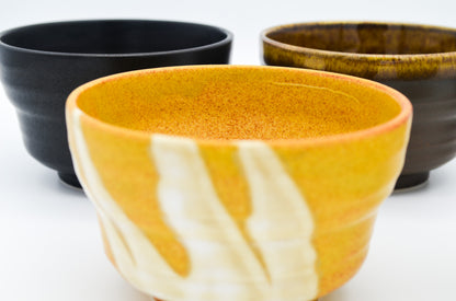 Three ceramic bowls in black, orange, and brown on a white background