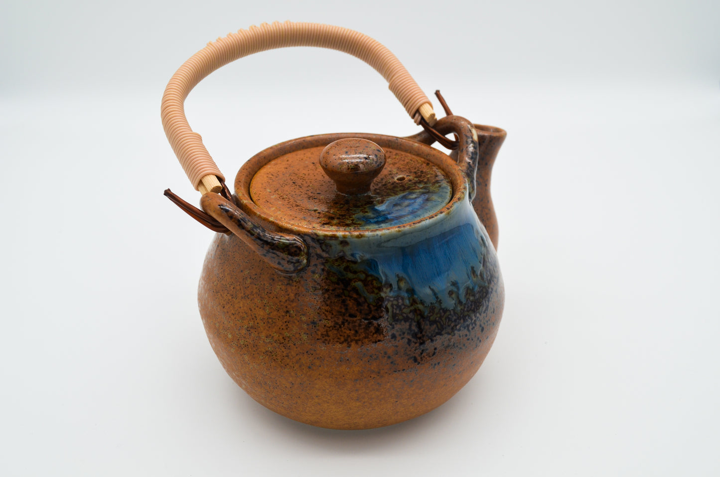 Ceramic teapot with a brown body and blue speckles on a white background