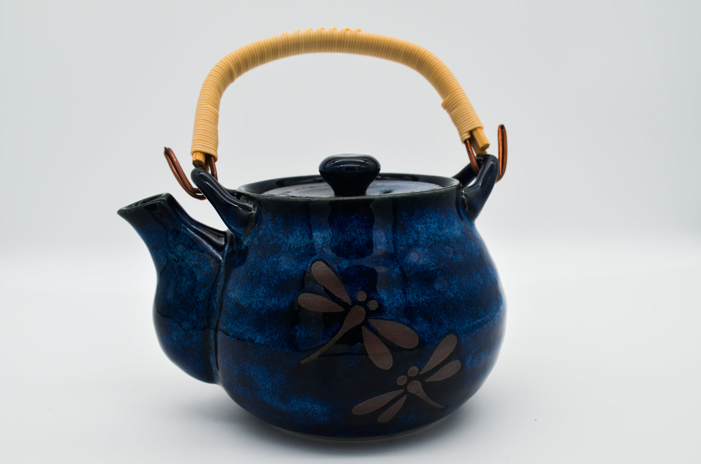 Blue ceramic teapot with dragonfly design and wooden handle on a white background