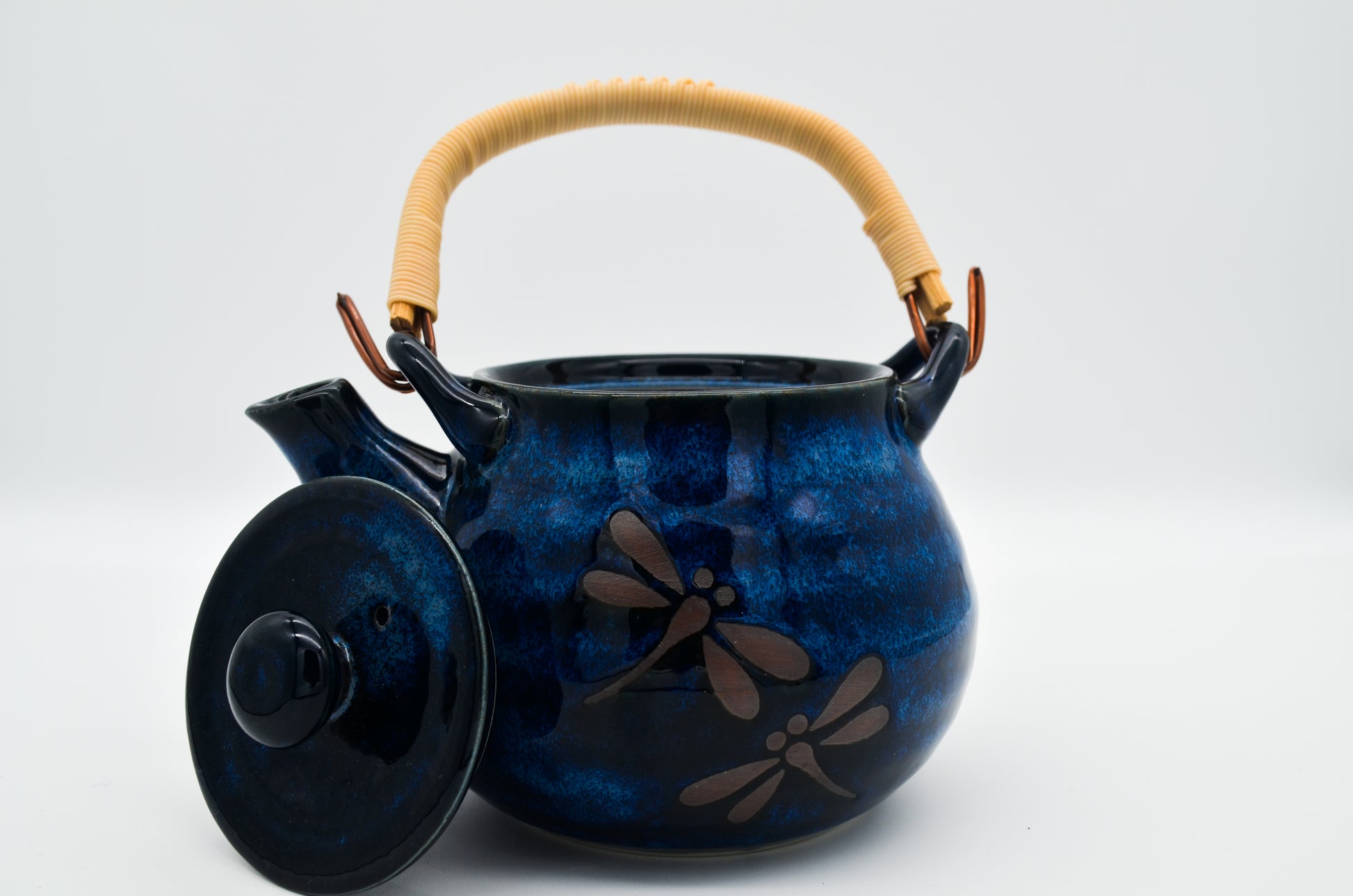 Blue ceramic teapot with dragonfly design and wooden handle on a white background