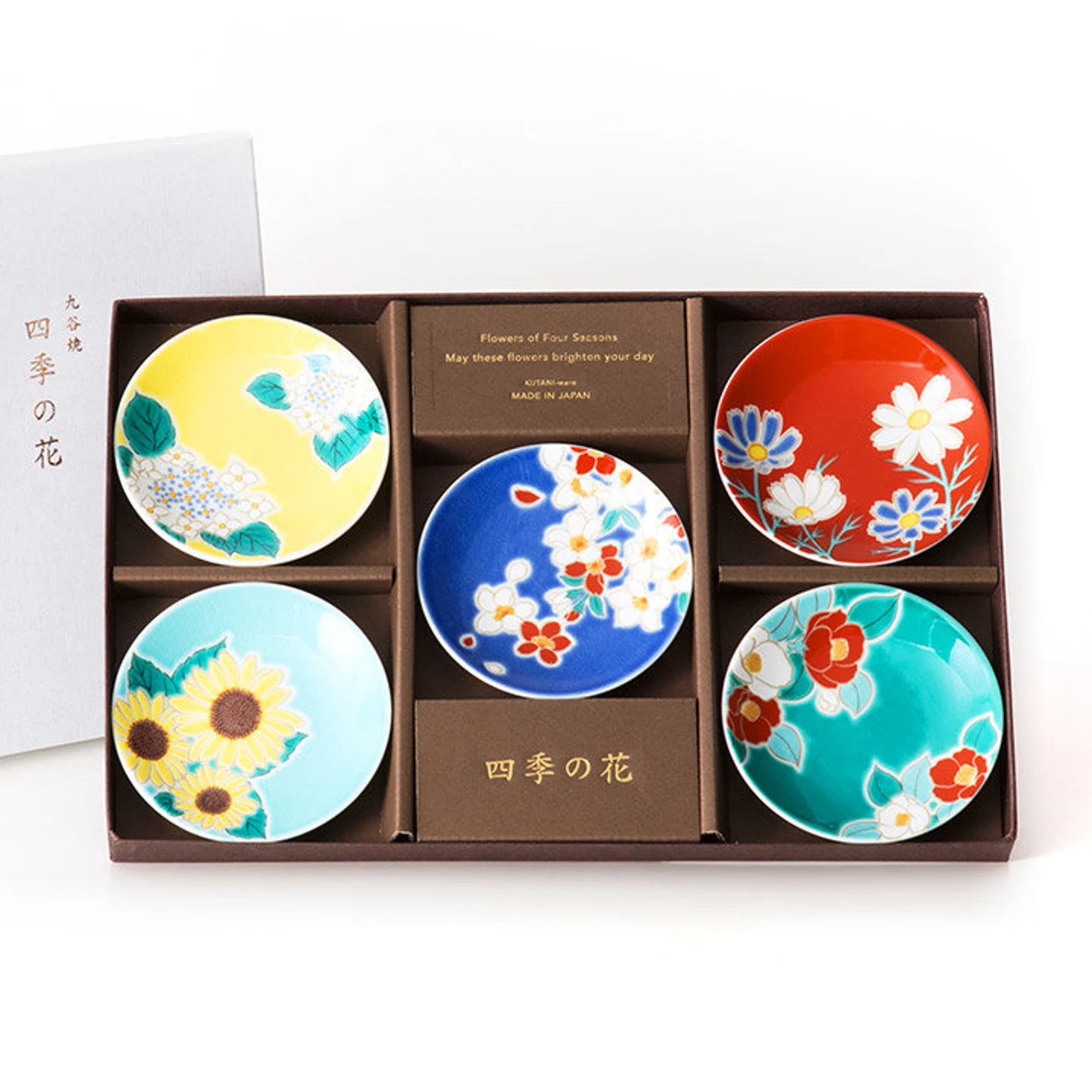 Set of five colorful ceramic plates in a box with floral designs on a white background.