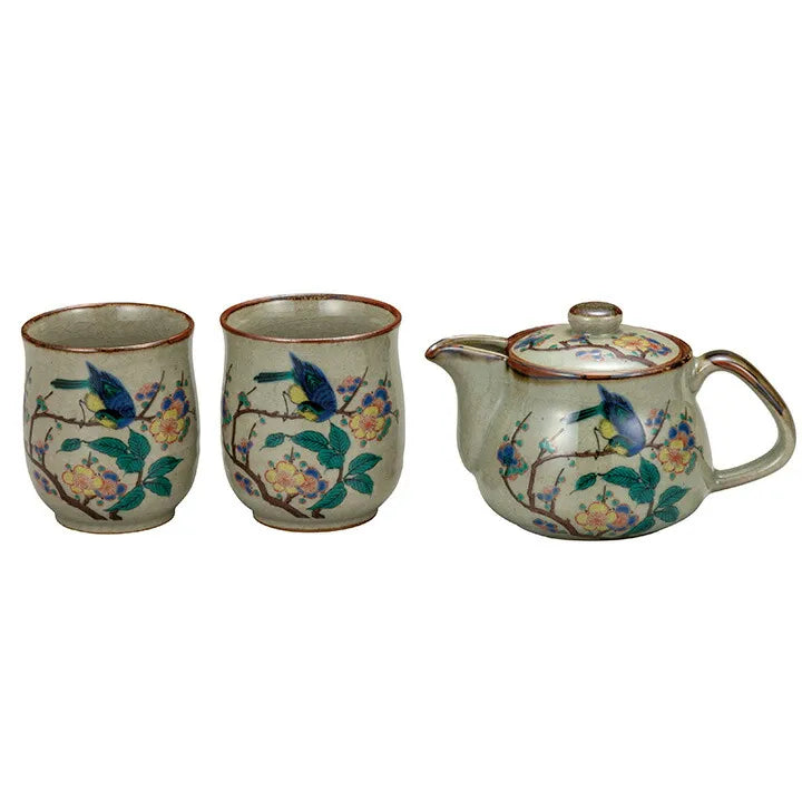 Ceramic teapot and two cups with bird and floral design on a white background