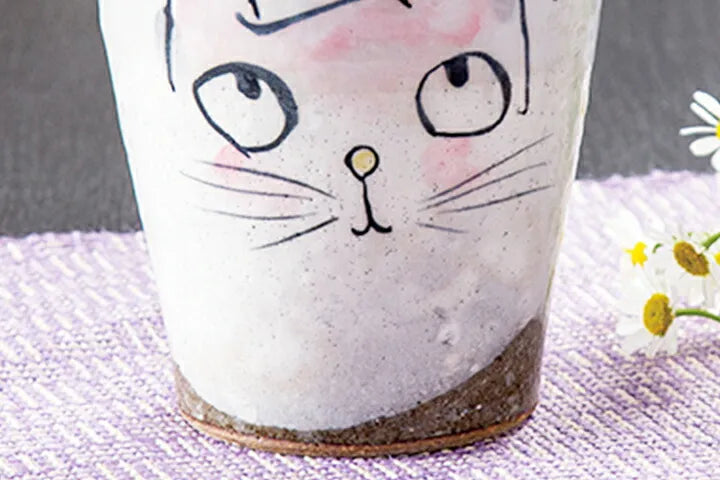 Ceramic cup with a cat face design on a textured surface.