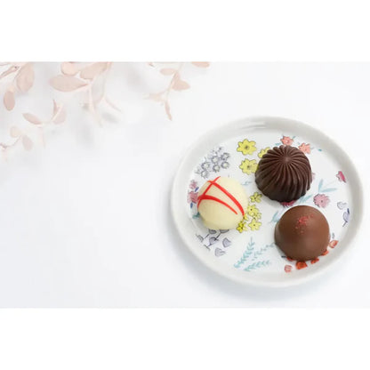 Three chocolate truffles on a decorative plate with floral patterns.