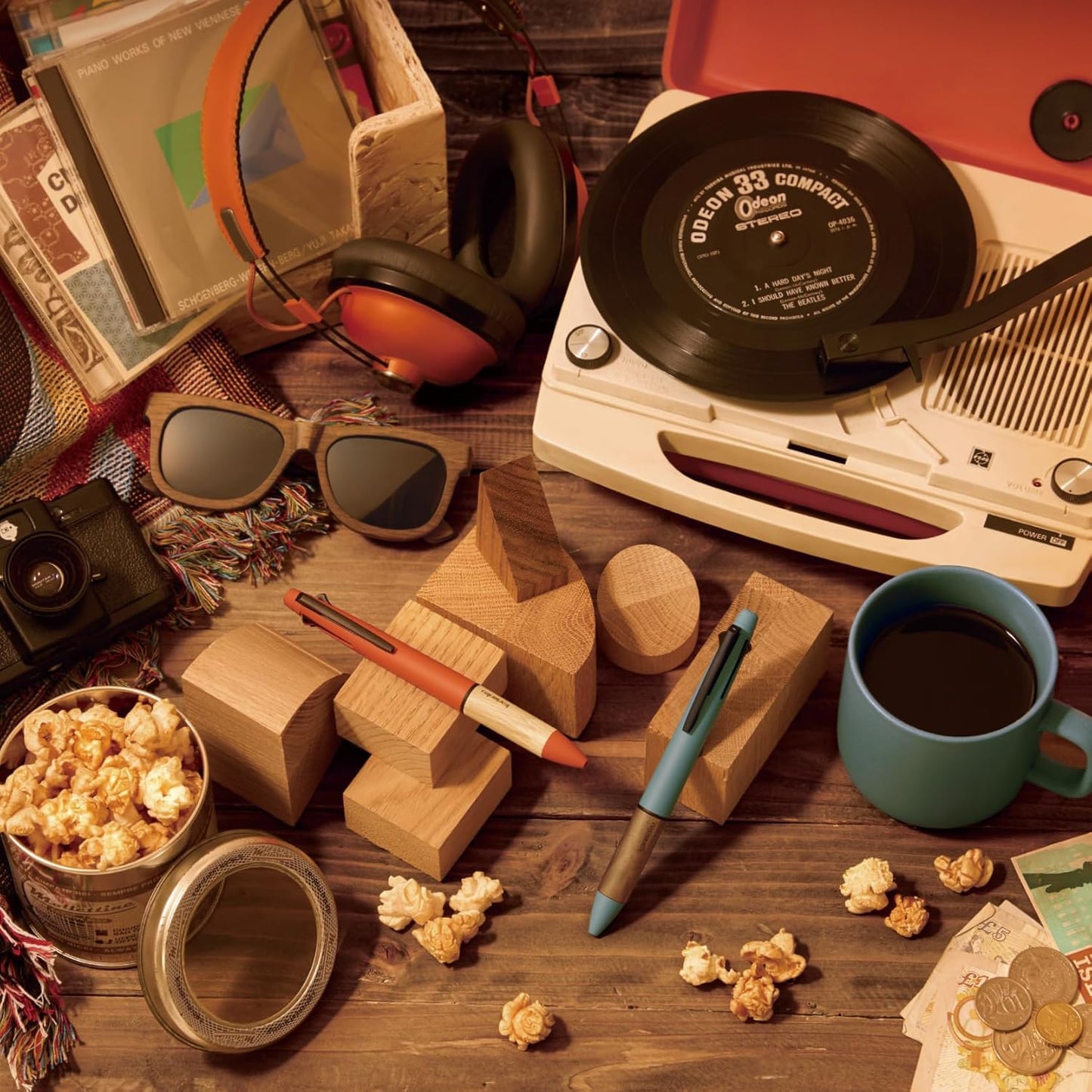 Vintage record player with vinyl record, coffee mug, popcorn, and sunglasses on a wooden table.