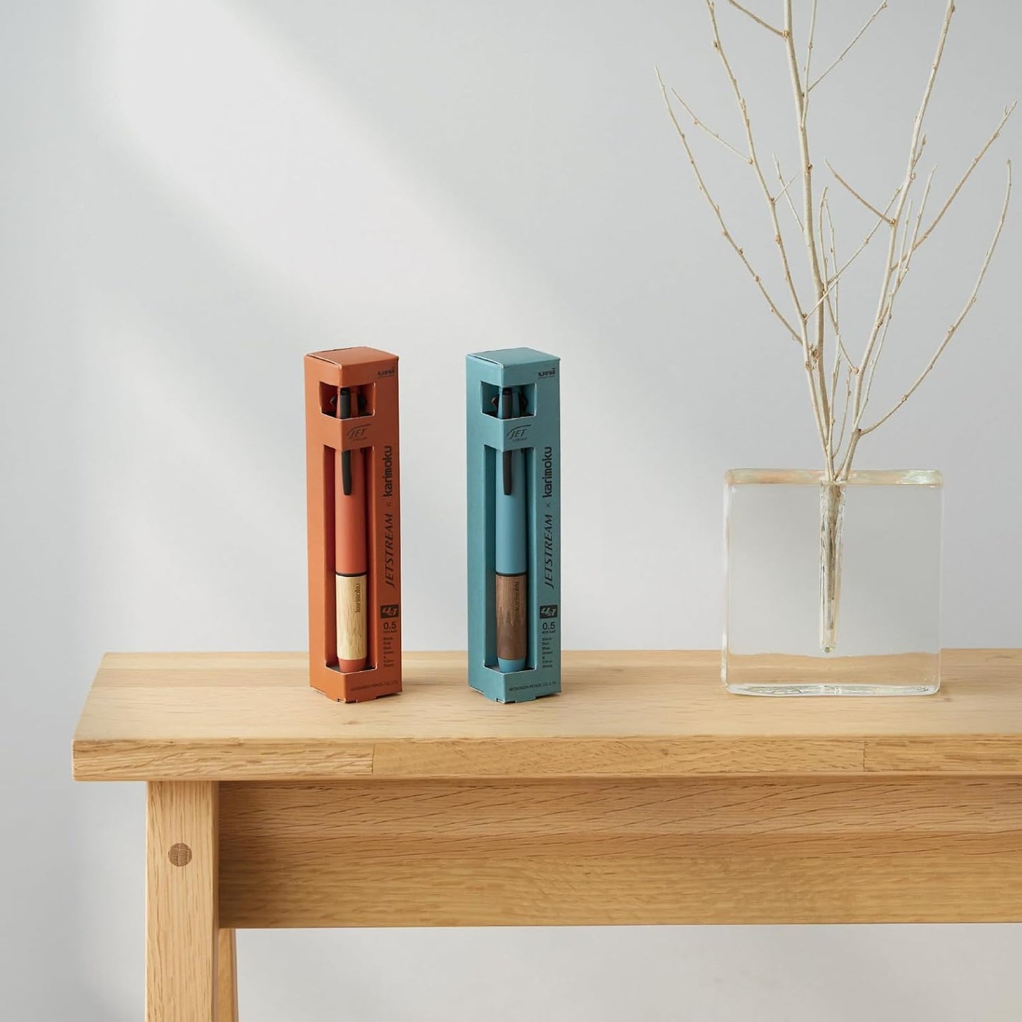 Two wooden products in packaging on a wooden table with a vase in the background.