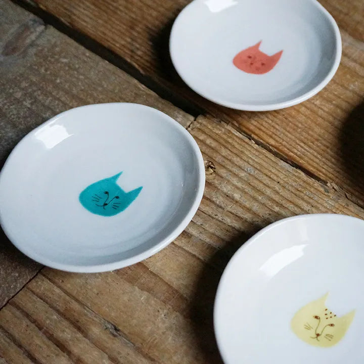 Three small white dishes with colorful cat illustrations on a wooden surface