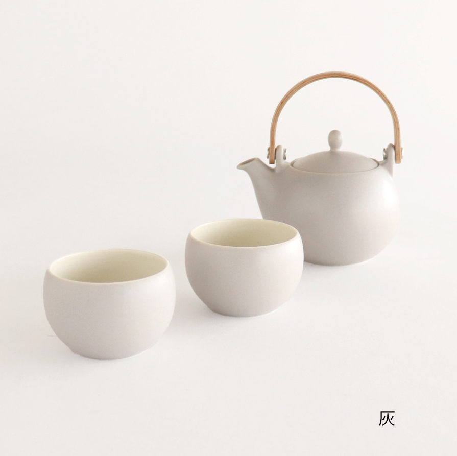 White ceramic teapot and two cups on a light gray background