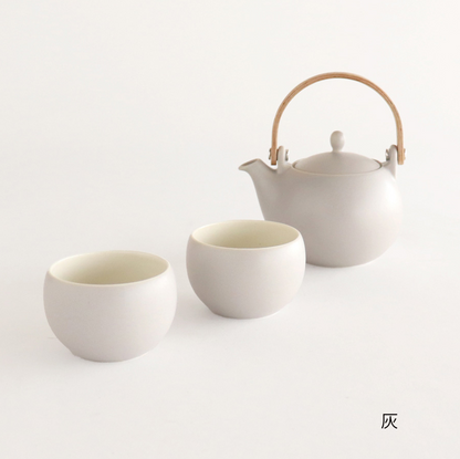 White ceramic teapot and two cups on a light gray background