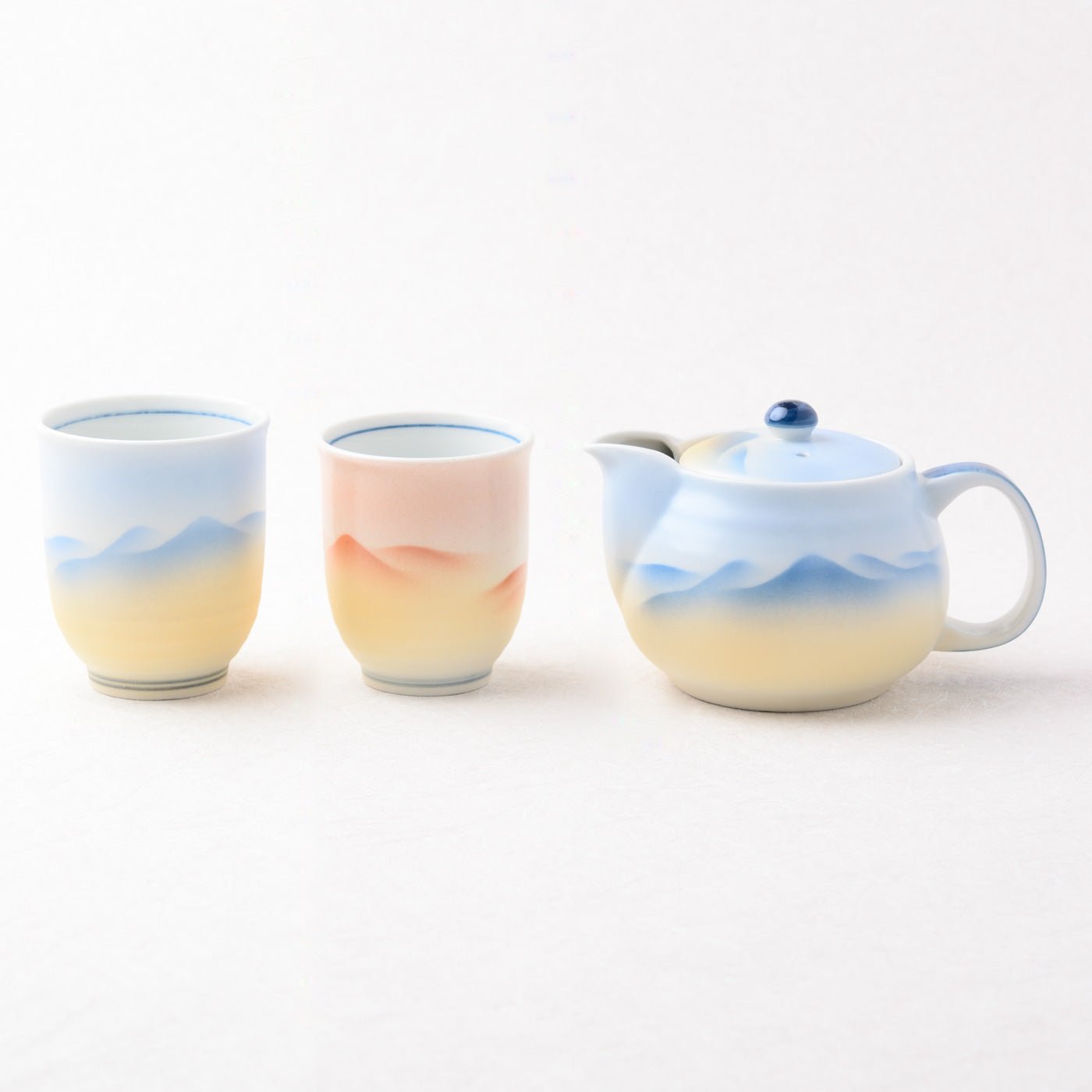 Set of ceramic tea cups and a teapot with mountain landscape design on a white background